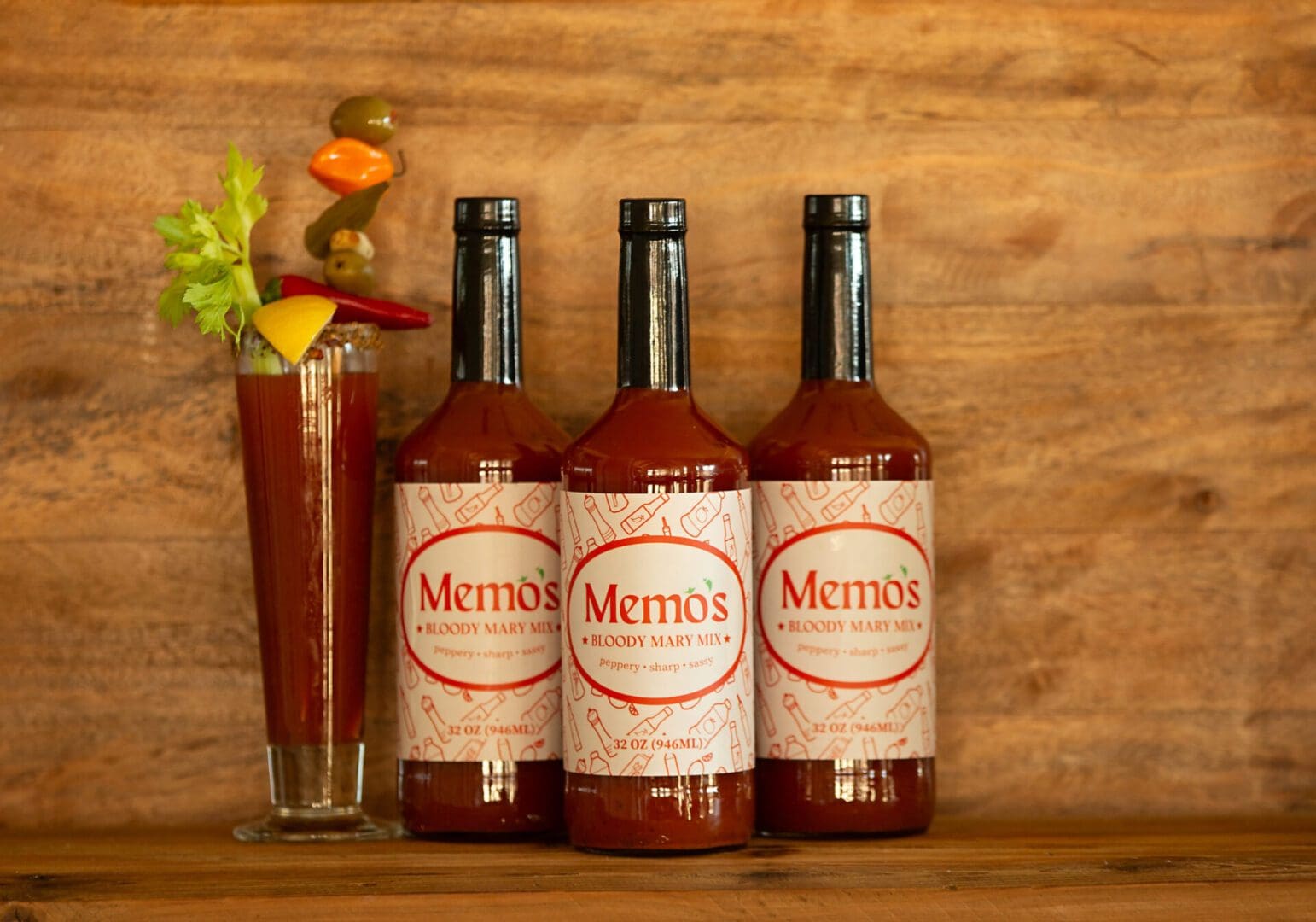 Three bottles of bloody mary sitting next to a glass.